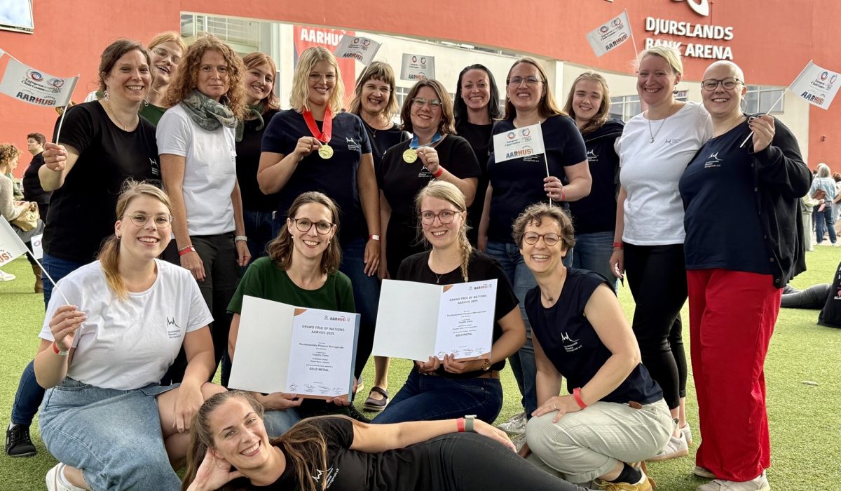 Eine Gruppe von Frauen posiert mit zwei Goldmedaillen und zwei Urkunden.